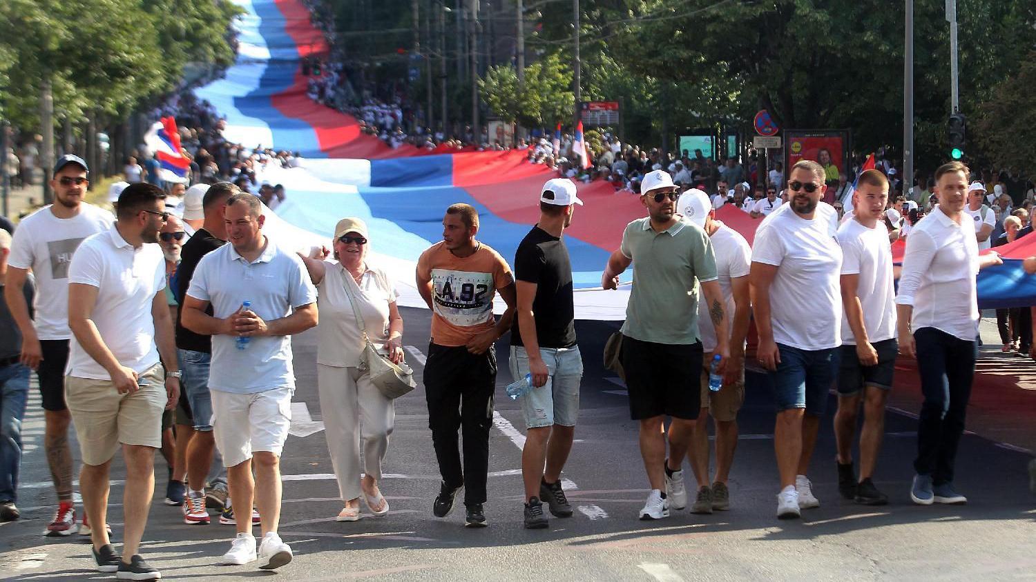 Ljudi hodaju ulicom, iza njih zastava Srbije