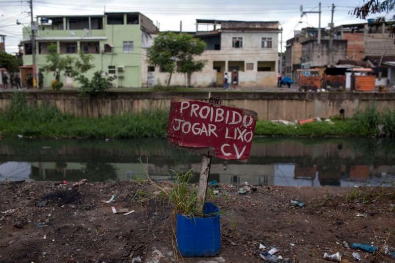 Placa em frente a valão diz 'Proibido jogar lixo - CV'