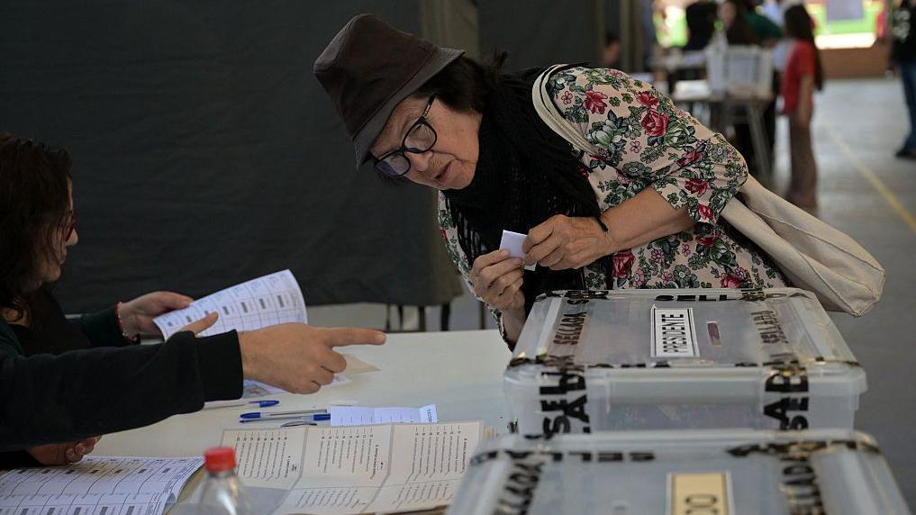 Una mujer se inclina ante una trabajadora de una mesa electoral que le da instrucciones antes de depositar su voto en un centro de votación de Santiago de Chile. 