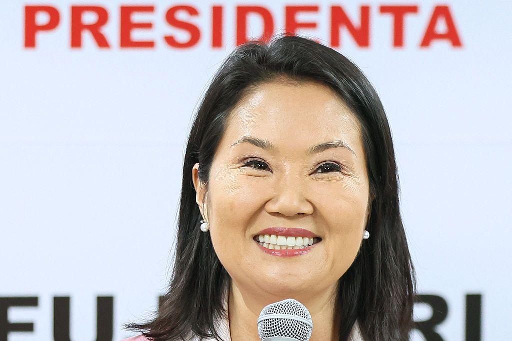 Keiko Fujimori sujeta sonriente un micrófono. Tras ella hay un cartel con el mensaje "Presidenta Fujimori". 