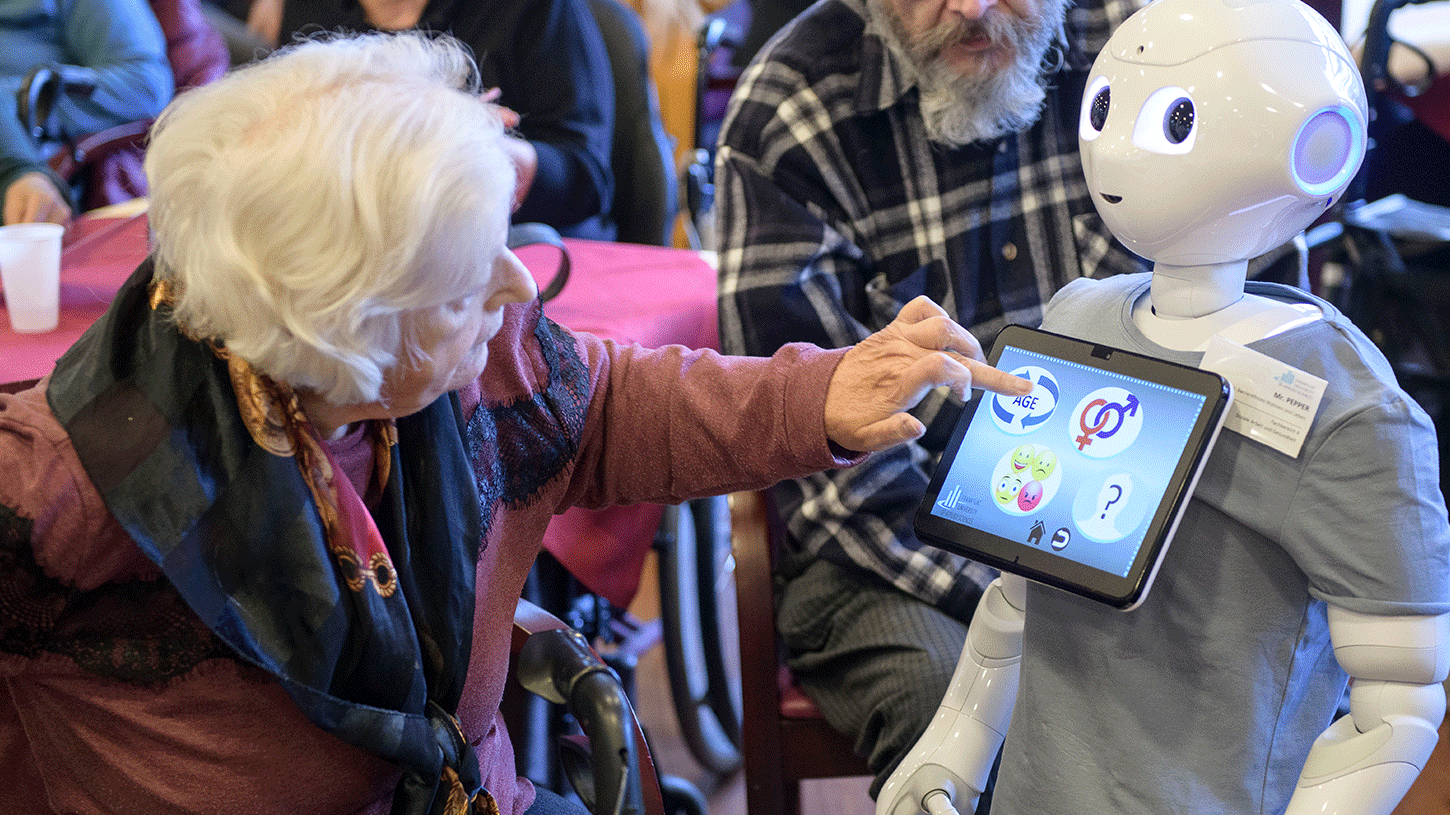 Uma mulher idosa olha para o robô e toca a tela em sua parte frontal.