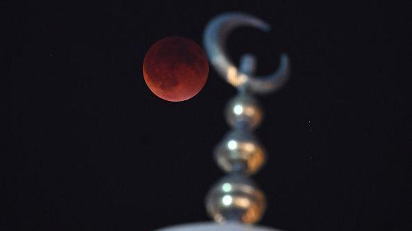 A lua cheia, de tom escuro e profundo, &eacute; fotografada acima de um minarete prateado na Cidade do Kuwait, no Kuwait.
