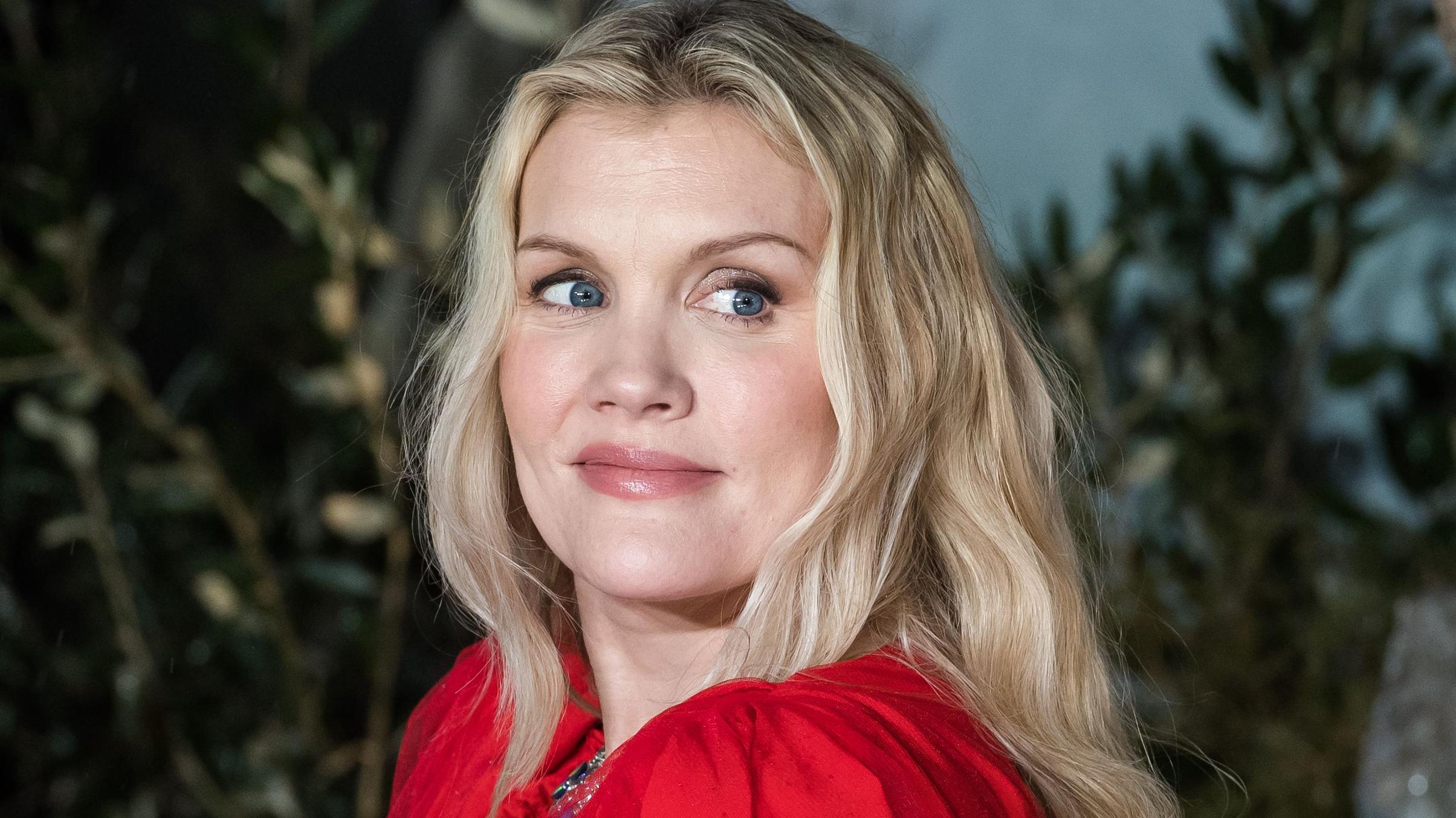  Emerald Fennell olha por cima do ombro na estreia de *Wuthering Heights* em Londres; ela tem longos cabelos loiros. 