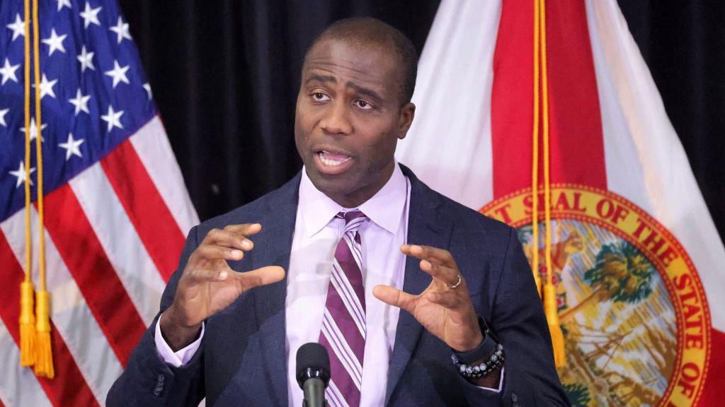 El cirujano general de Florida, Joseph Ladapo, habla en una rueda de prensa en abril de 2024. Viste traje azul, camisa clara y corbata de rayas.