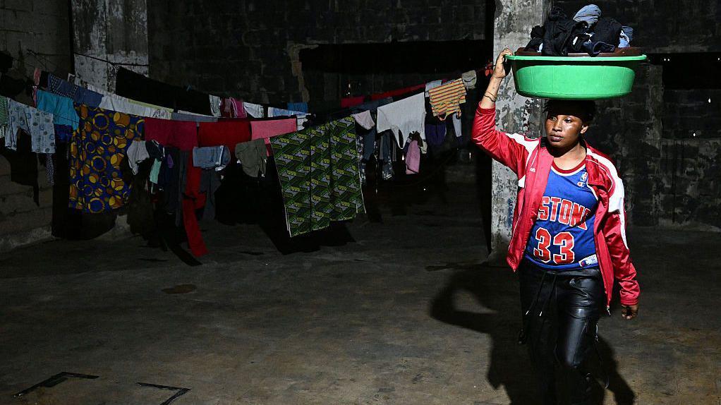 سيدة من أثيوبيا في مرآب تحمل سلة ملابس وخلفها ثياب معلقة على حبل غسيل