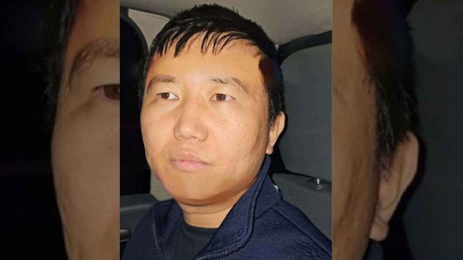 Primer plano de Zhi Dong Zhang en lo que parece el interior de un auto, vestido con ropa deportiva, chaqueta azul oscura y camiseta negra.