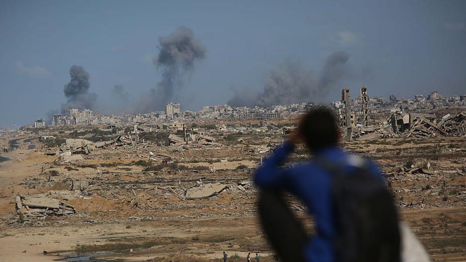 Una persona sentada en un montículo observa las columnas de humo en la distancia de los ataques israelíes en Ciudad de Gaza.