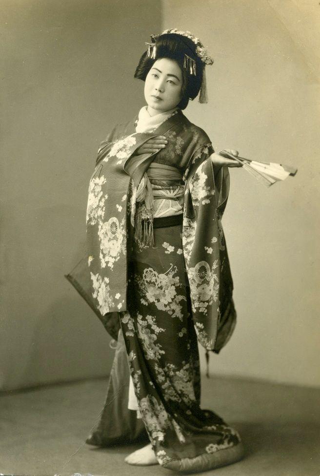 Una japonesa vestida con un kimono con flores y un abanico en la mano.