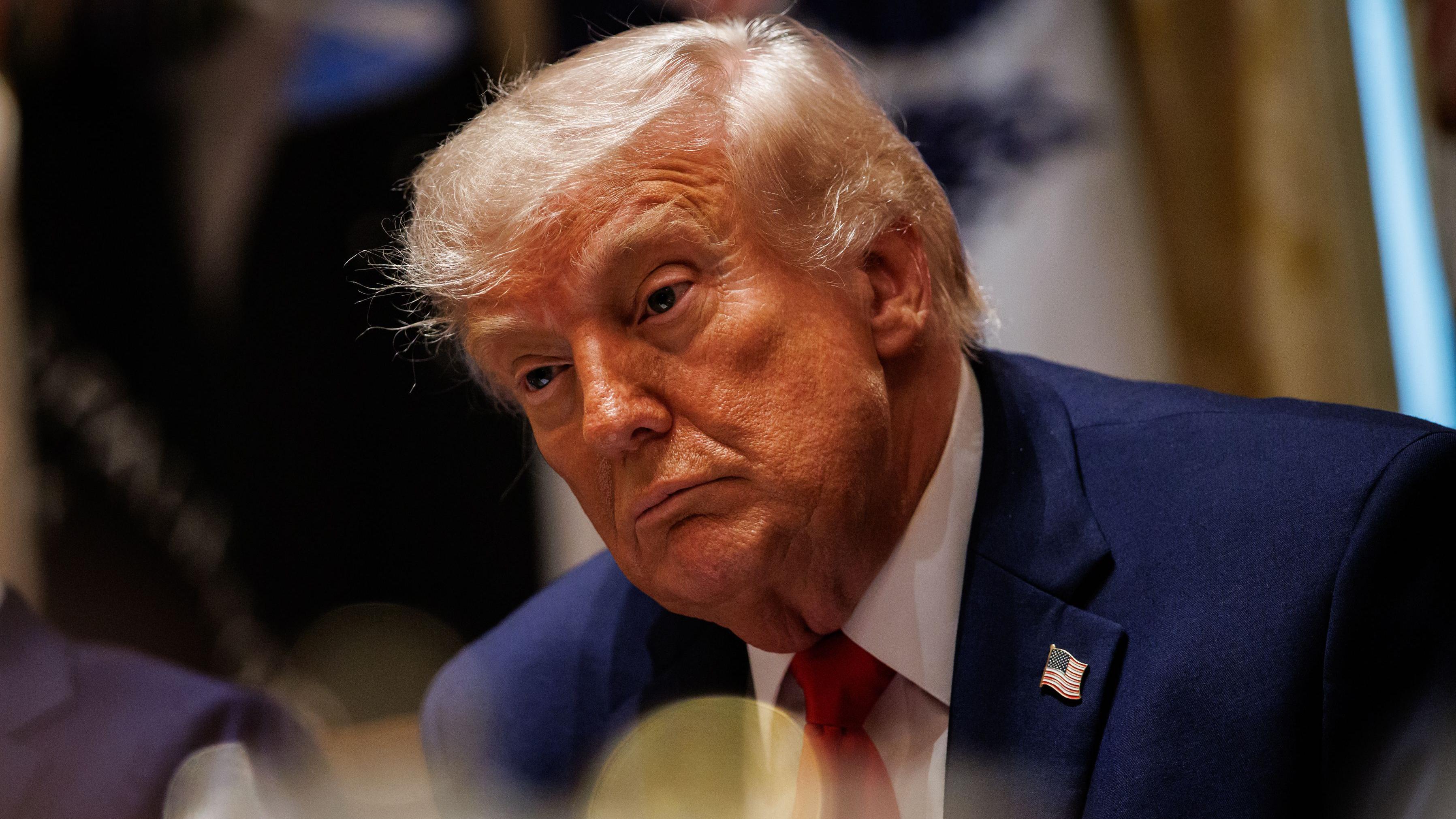 O presidente dos EUA, Donald Trump, em um terno azul marinho e uma gravata vermelha, observa o interior da Sala do Gabinete da Casa Branca