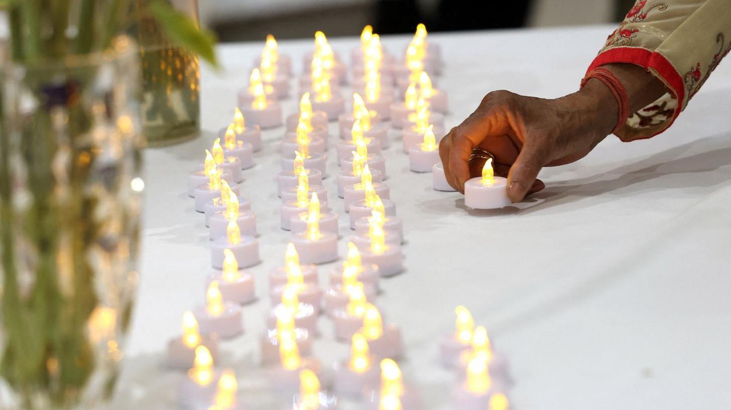 Uma mulher acende uma vela ao lado de fileiras de outras velas