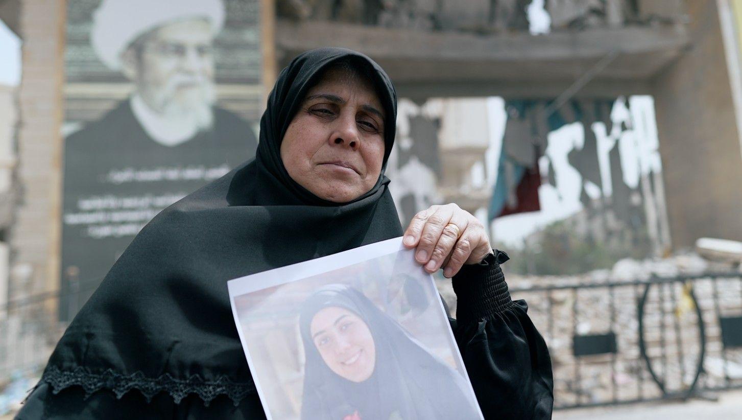 امرأة محجبة ترفع صورة لإحدى بناتها المتوفيات

