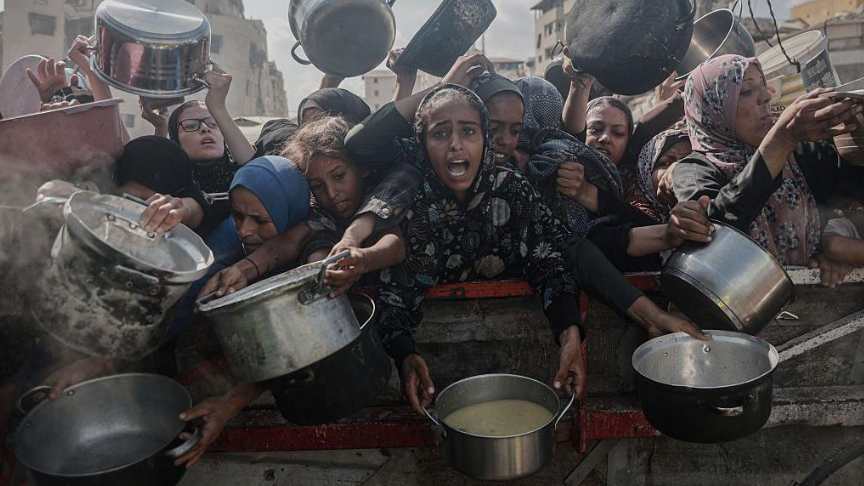 مجموعة من النساء الفلسطينيات ترتدين ملابس إسلامية الطابَع وتمسكن بأوانٍ فارغة، على أمل ملئها بالغذاء من أحد مراكز توزيع المساعدات الغذائية، وسط الحصار والهجمات الإسرائيلية المتواصلة على غزة.