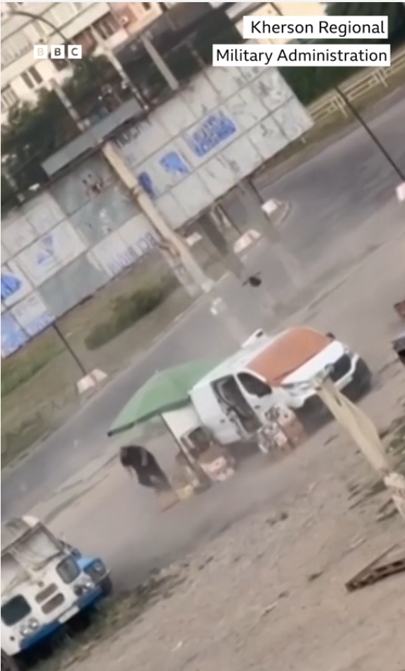 طائرة مسيرة تهاجم بائع خضروات أوكراني يرتدي ملابس سوداء بينما يحاول الهرب منها في منطقة تقف فيها سيارات تبيع الخضروات.