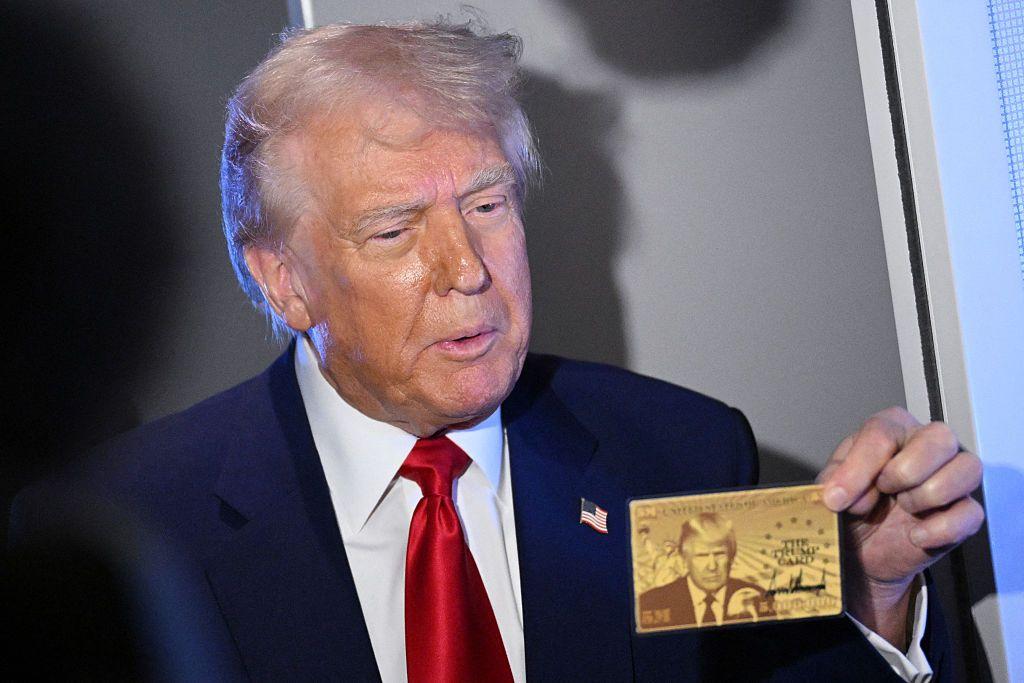 Donald Trump sujeta con su mano izquierda una tarjeta dorada con su efigie. 