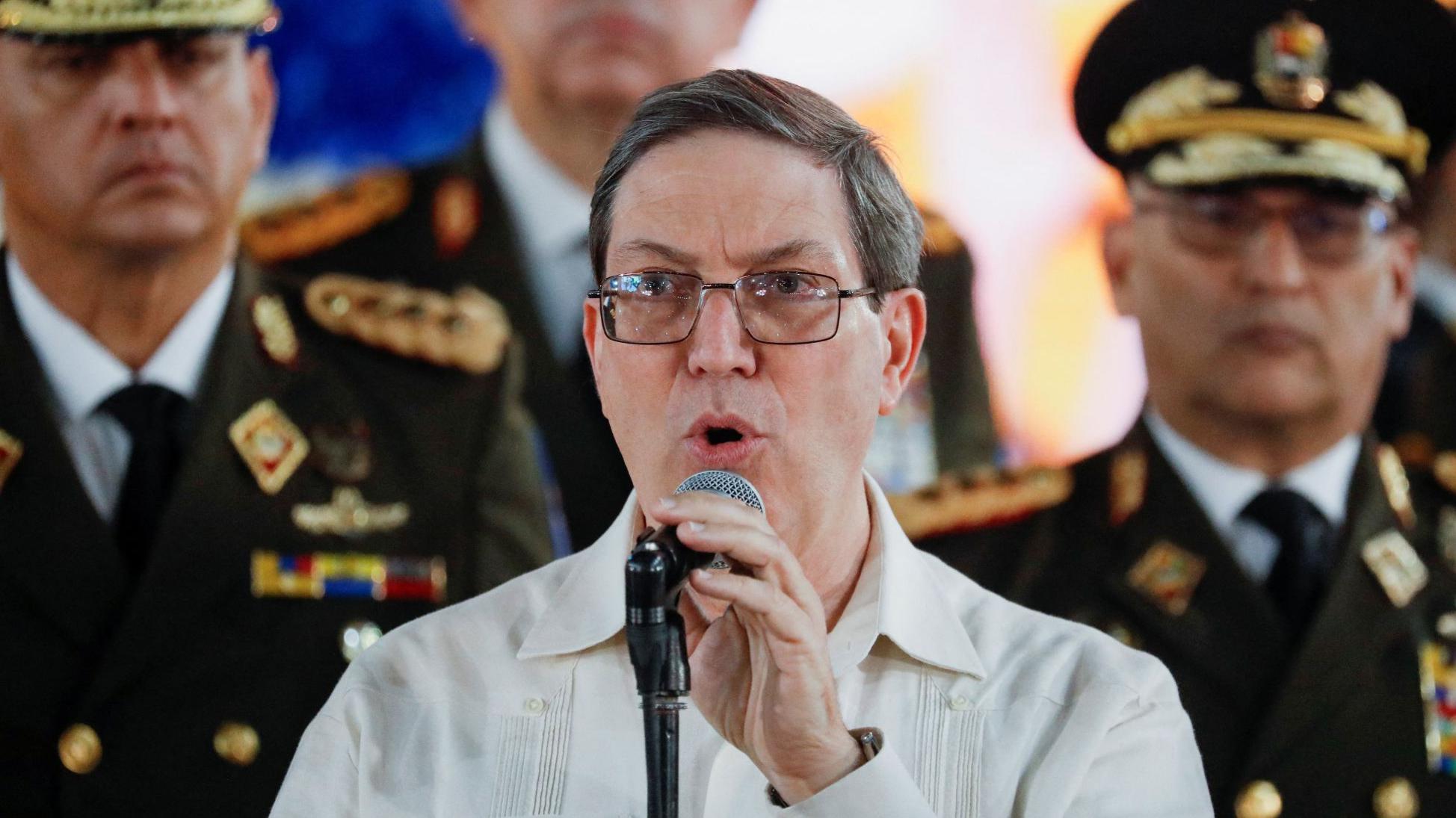 El canciller de Cuba, Bruno Rodríguez. habla ante un micrófono acompañado de oficiales militares