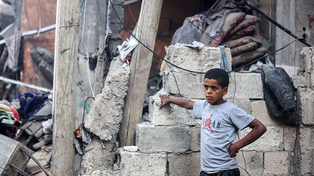 "أسوأ من البدء من الصفر": ما حجم مهمة إعادة إعمار غزة؟ 2 طفل فلسطيني ينظر إلى رجل يبحث عن ناجين بين أنقاض مبنى في مخيم الشاطئ للاجئين بمدينة غزة، في 9 يوليو/تموز 2025، والذي استُهدف بغارة إسرائيلية.