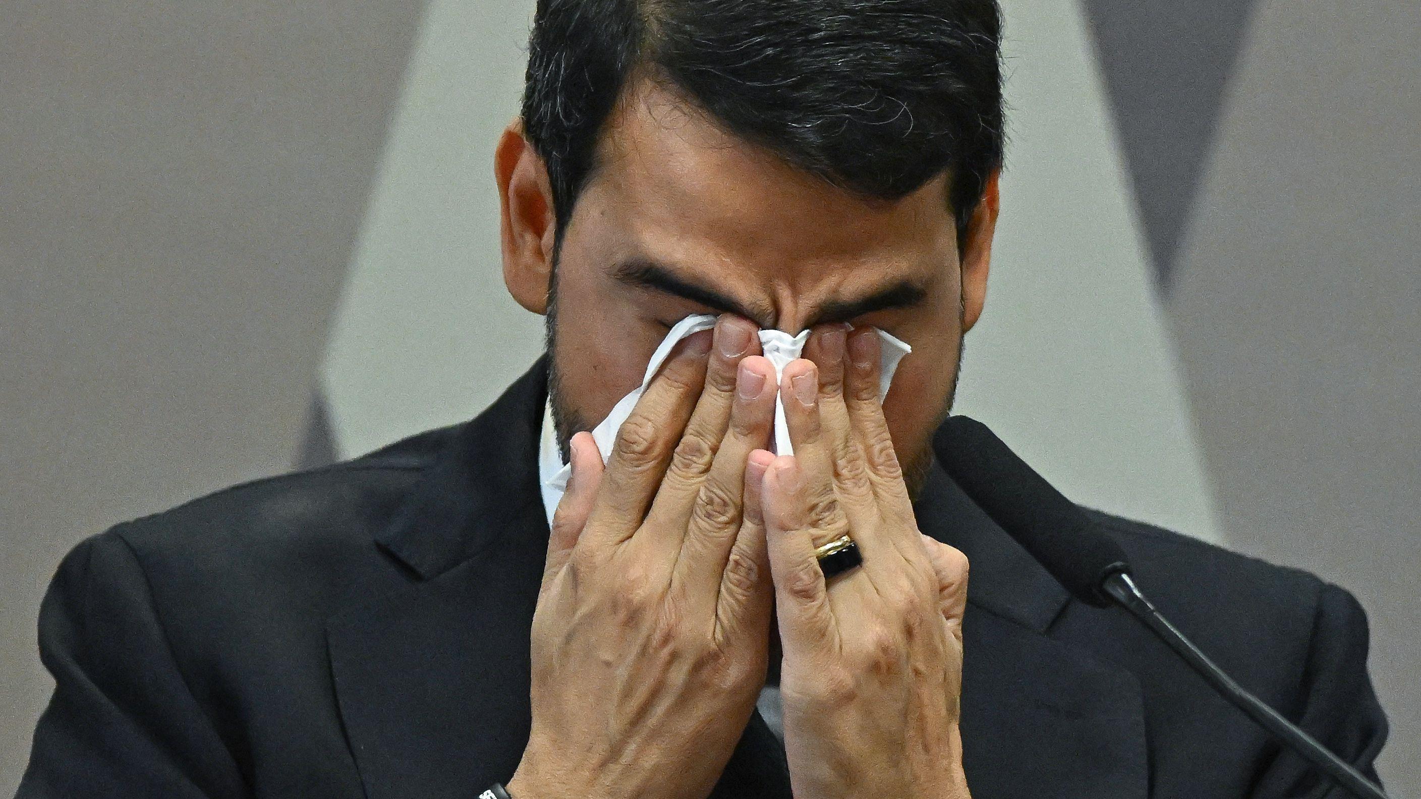 Jorge Messias enxuga o rosto, cobrindo sua face com as duas m&atilde;os.