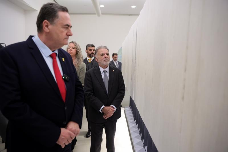 Em destaque, dois homens engravatados e braços contidos observam parede de museu