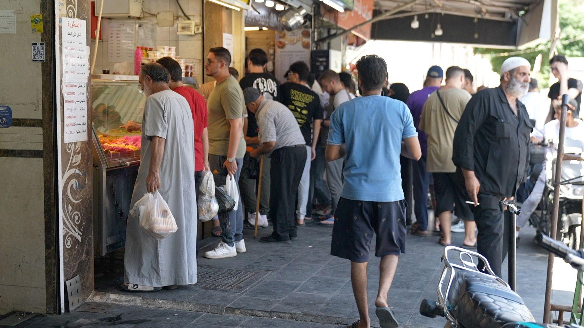 مجموعة من الناس يتجولون في السوق ويشتؤون بعضاً من احتياجاتهم.