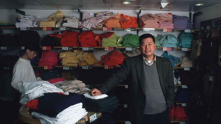 1993年拍攝的照片中，黎智英身穿灰色背心與西裝外套，站在佐丹奴門市內，身後是擺滿彩色T恤的貨架。