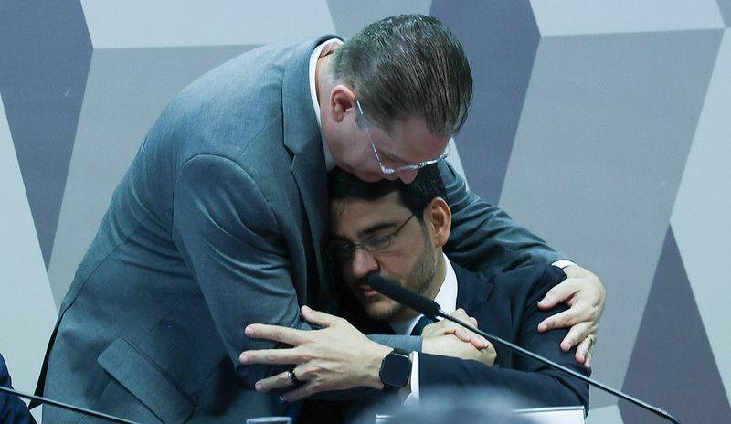 Jorge Messias, sentado, recebe abra&ccedil;o do l&iacute;der do PL na C&acirc;mara dos Deputados,  S&oacute;stenes Cavalcante, durante sess&atilde;o de sabatina no Senado. Na foto, Messias aparece de olhos fechados, em postura contemplativa enquanto &eacute; abra&ccedil;ado com os dois bra&ccedil;os pelo deputado 