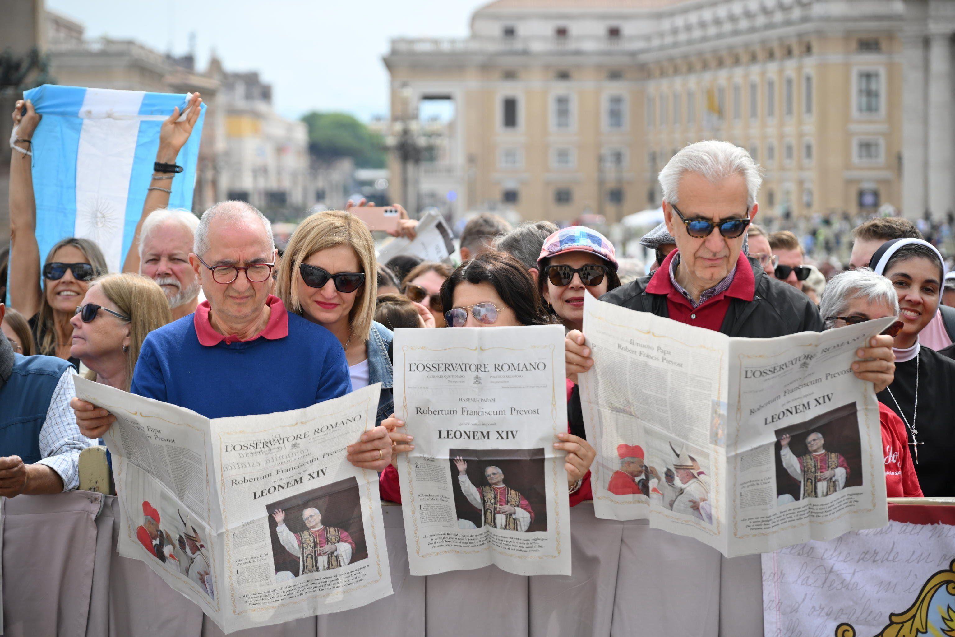 Feligreses y turistas revisan la edición especial del diario vaticanista L'Osservatore Romano.