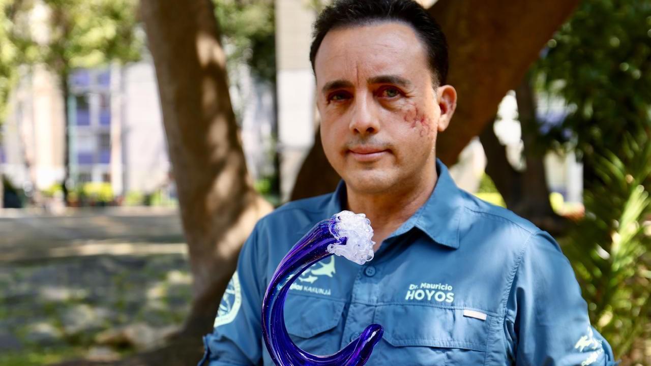 Mauricio mira a la cámara, mientras sostiene un premio en forma de ola. 