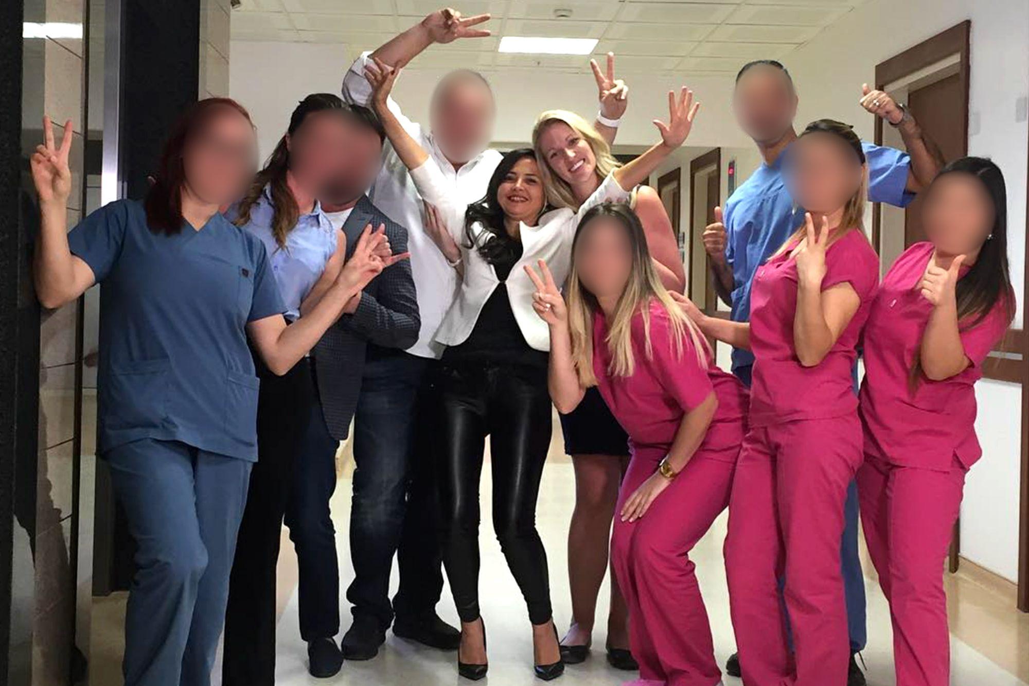 Grupo de 10 pessoas reunidas em um corredor, algumas usando roupas m&eacute;dicas, posando com as m&atilde;os erguidas e fazendo gestos.