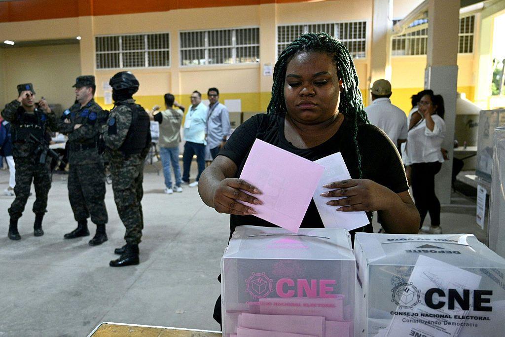 Una mujer votando en las elecciones presidenciales de Honduras el pasado 30 de noviembre y atrás unos militares que custodian el centro.