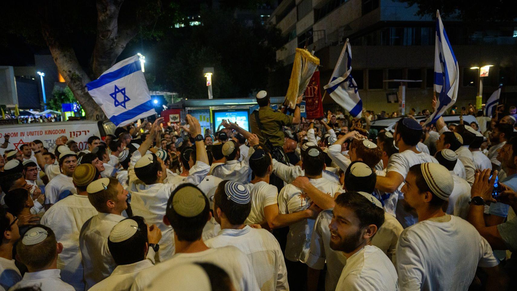 جندي من الجيش الإسرائيلي، برفقة مصلين آخرين، يحمل توراة ويحتفلون بطقس "هاكافوت" (عيد سيمحات توراة)، في اليوم الذي أُطلق فيه سراح أربع جثث أخرى من الأسرى، وفي اليوم التالي لإطلاق سراح عشرين رهينة أحياء، في ساحة الأسرى في تل أبيب، إسرائيل