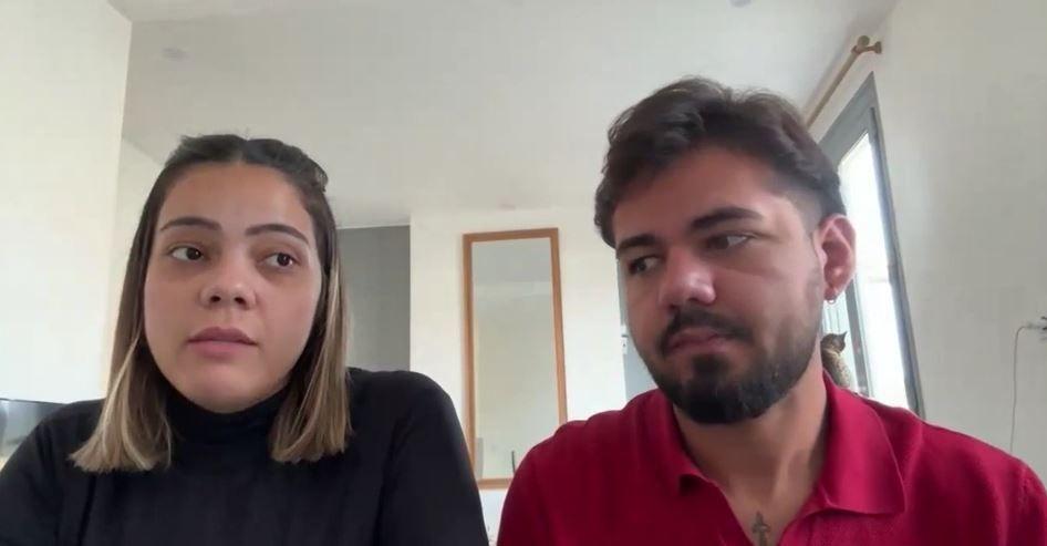 Uma mulher e um homem um ao lado do outro. Ela usa uma blusa preta e ele uma blusa vermelha