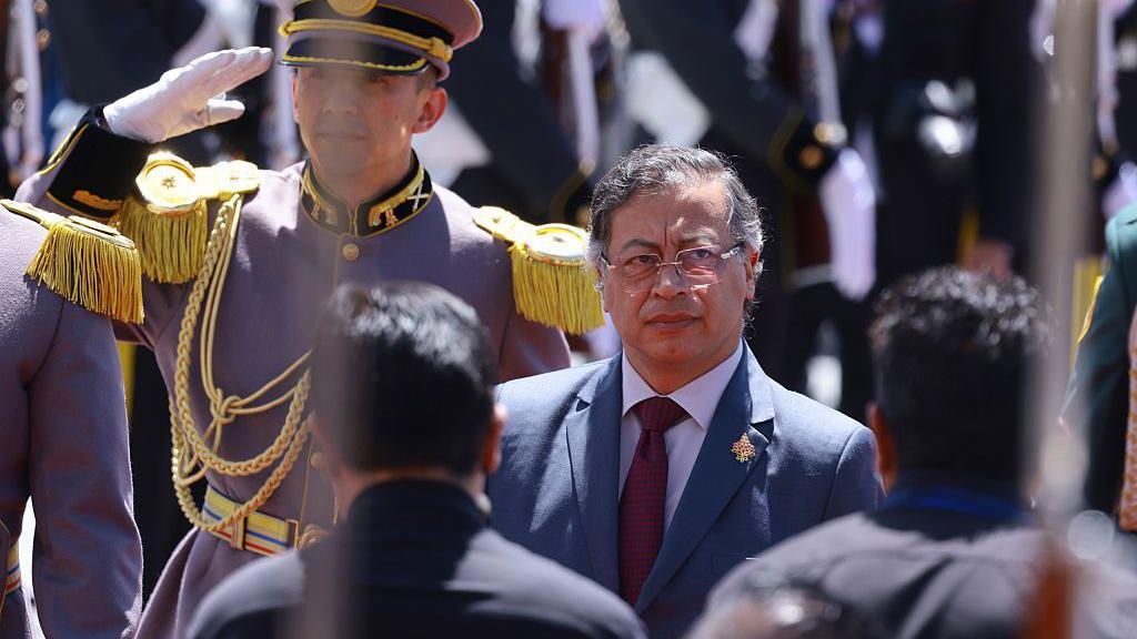 Gustavo petro de pie entre varios militares que realizan un saludo oficial. 