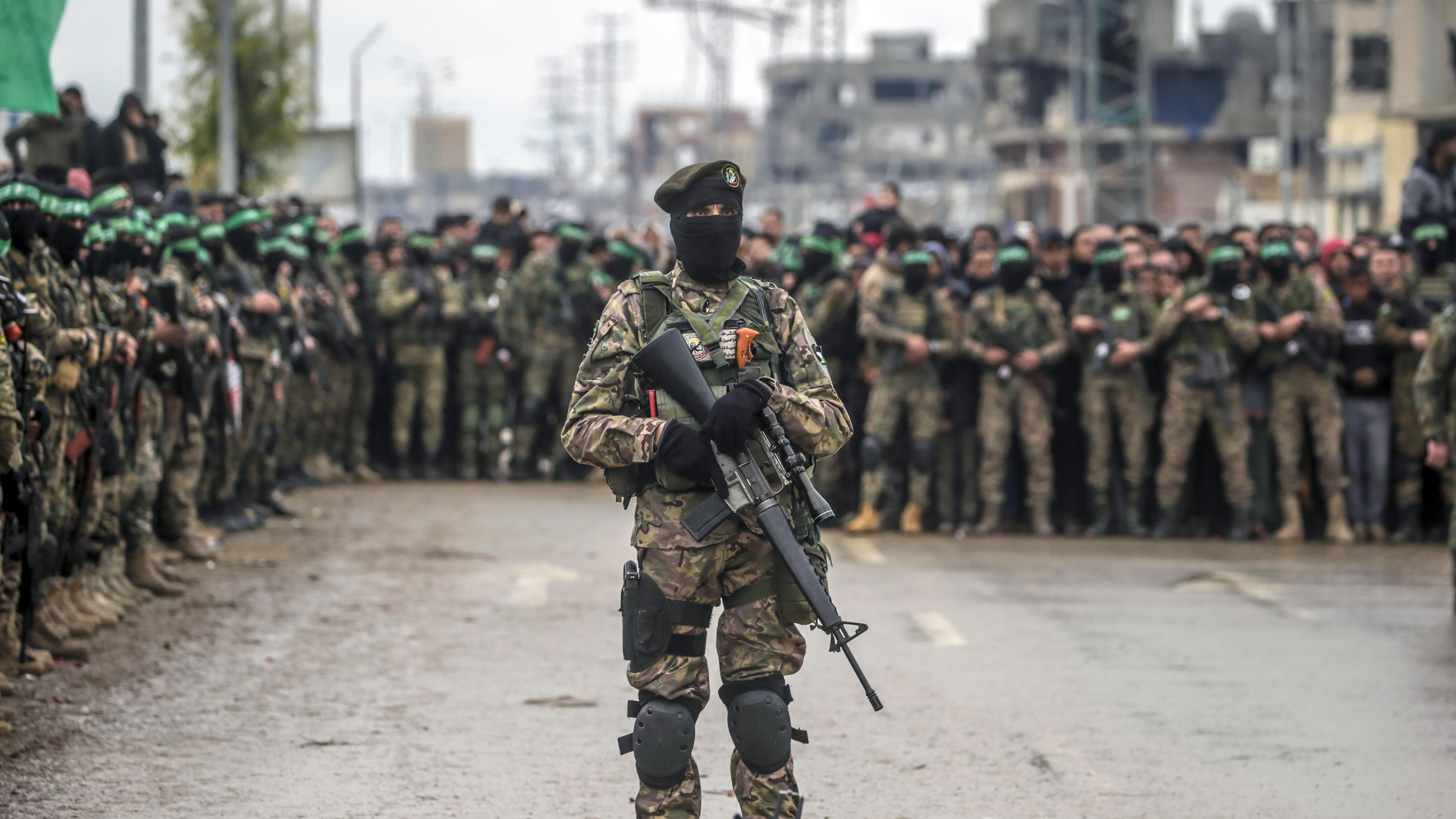 مقاتلون مسلحون من كتائب عز الدين القسام التابعة لحماس يقفون حراساً أثناء تسليم ثلاثة رهائن إسرائيليين إلى ممثلي الصليب الأحمر في مخيم النصيرات للاجئين، وسط قطاع غزة، 22 فبراير/ شباط 2025. 