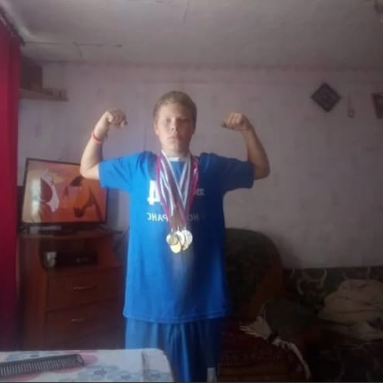 Menino com uma roupa azul e diversas medalhas esportivas penduradas no peito.