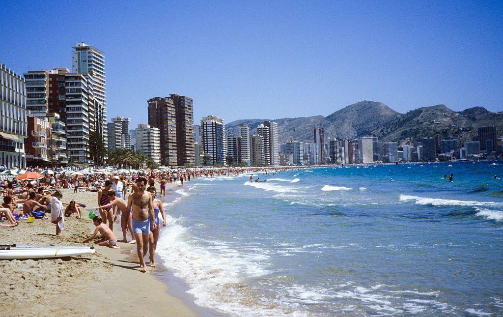 Vista de Benidorm desde la playa, con turistas bañándose y rascacielos.
