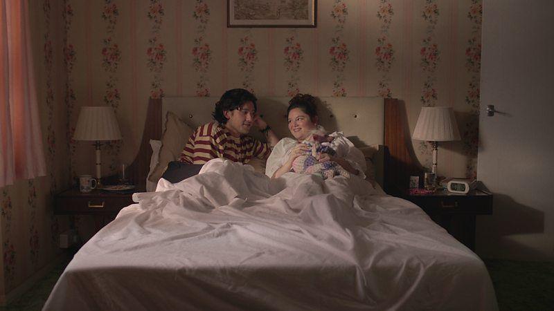 Casal deitado na cama em cena de 