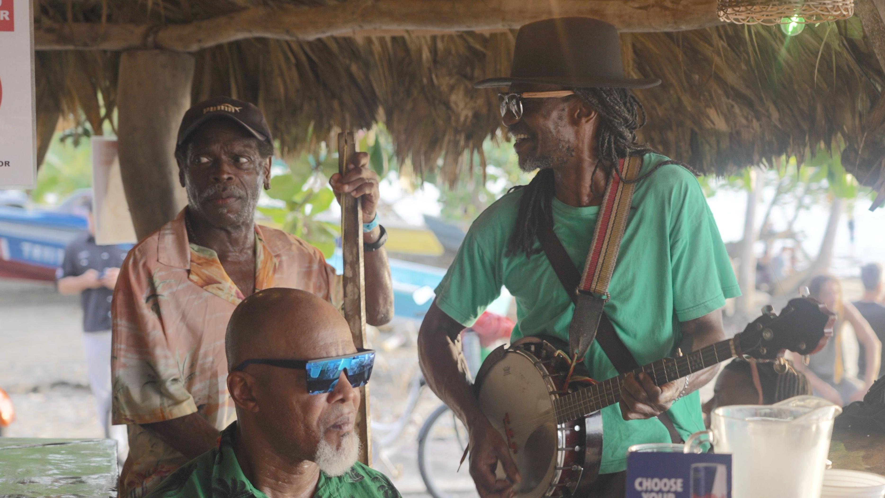 Tres músicos afrocaribeños interpretan música de calipso en un restaurante frente al mar en Puerto Viejo de Talamanca, Costa Rica, durante el atardecer.
