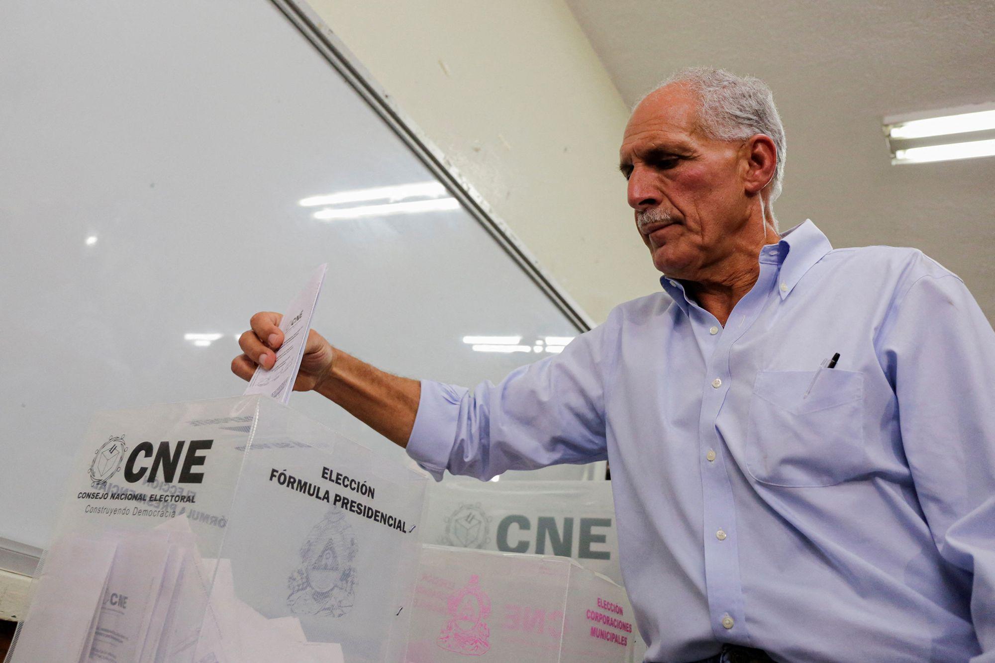 Nasry "Tito" Asfura coloca su voto en la urna del CNE. Detrás se ve un pizarrón de aula escolar.