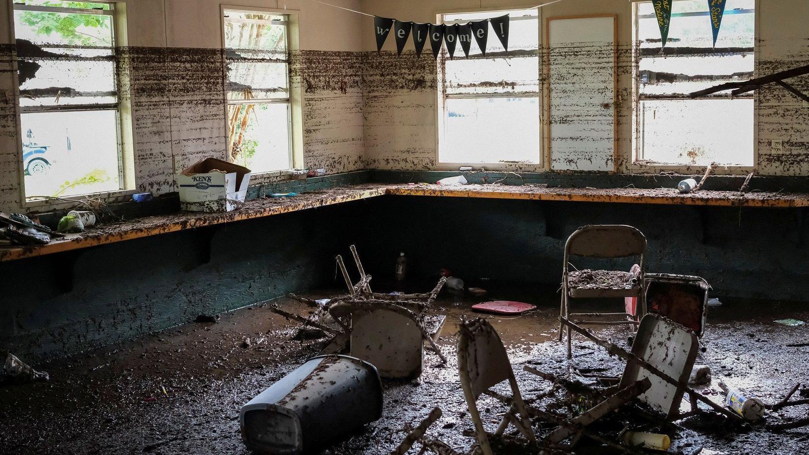 Imagem de uma sala com cadeiras jogadas cheia de lama.