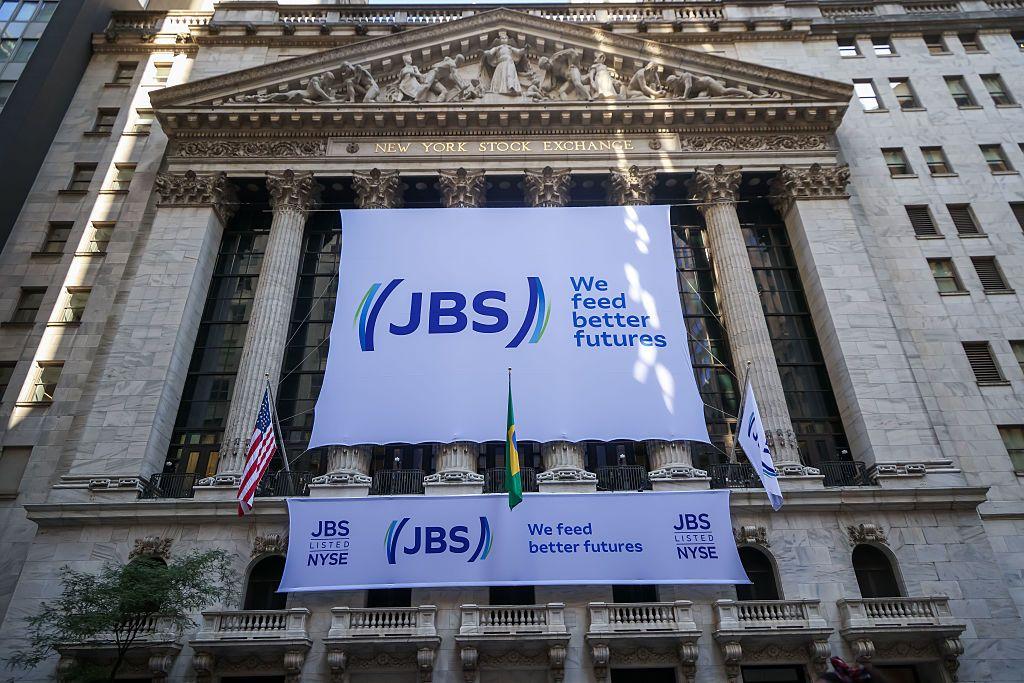 Dos grandes letreros blancos con el logo de JBS y el lema "Alimentamos mejores futuros" escritos en blanco, en la fachada del edificio de la Bolsa de Nueva York