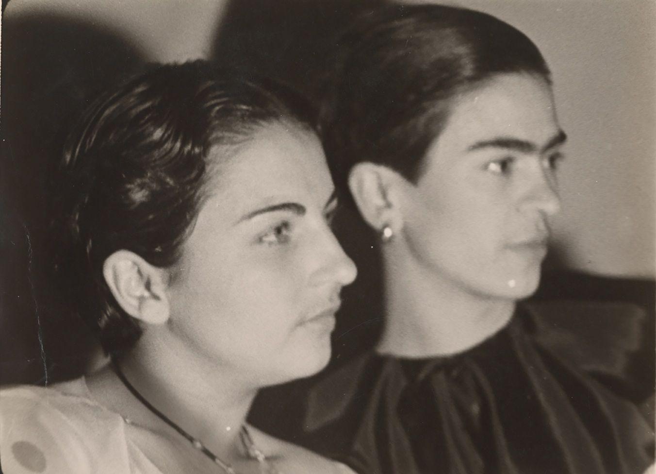 Perfil del rostro de Cristina, que tiene una blusa blanca y un collar. A su lado, de fondo, está Frida, que tiene una blusa negra y aretes. También está de perfil.

