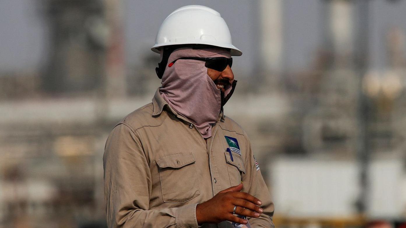 Trabalhador de plataforma petrol&iacute;fera, com capacete branco e uniforme de trabalho c&aacute;qui, olha para o lado