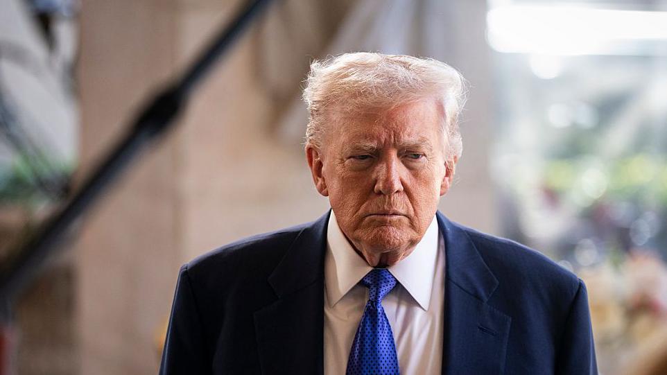 Donald Trump, con traje oscuro, corbata azul y gesto pensativo. 