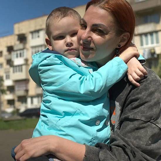 Oleana abrazando a su hija Viktoriia. La niña, con un abrigo celeste y el pelo muy corto, tiene ambos brazos alrededor del cuello de su madre