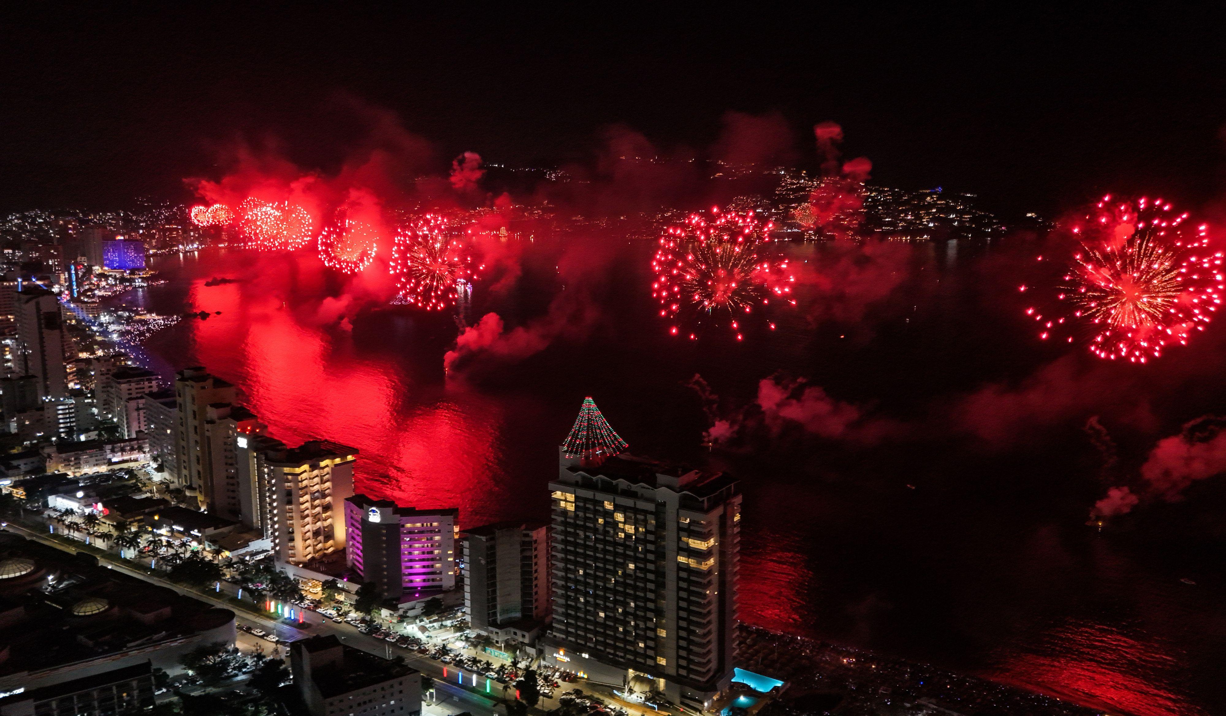 Una explosión de fuegos artificiales rojos iluminan la bahía de Acapulco