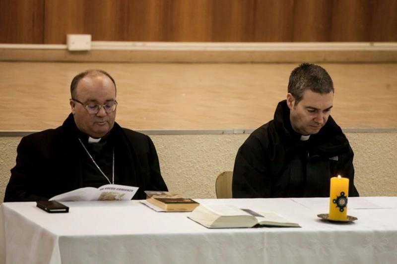 Los sacerdotes Charles Scicluna y Jordi Bertomeu, sentados en una mesa con una vela y algunos libros.