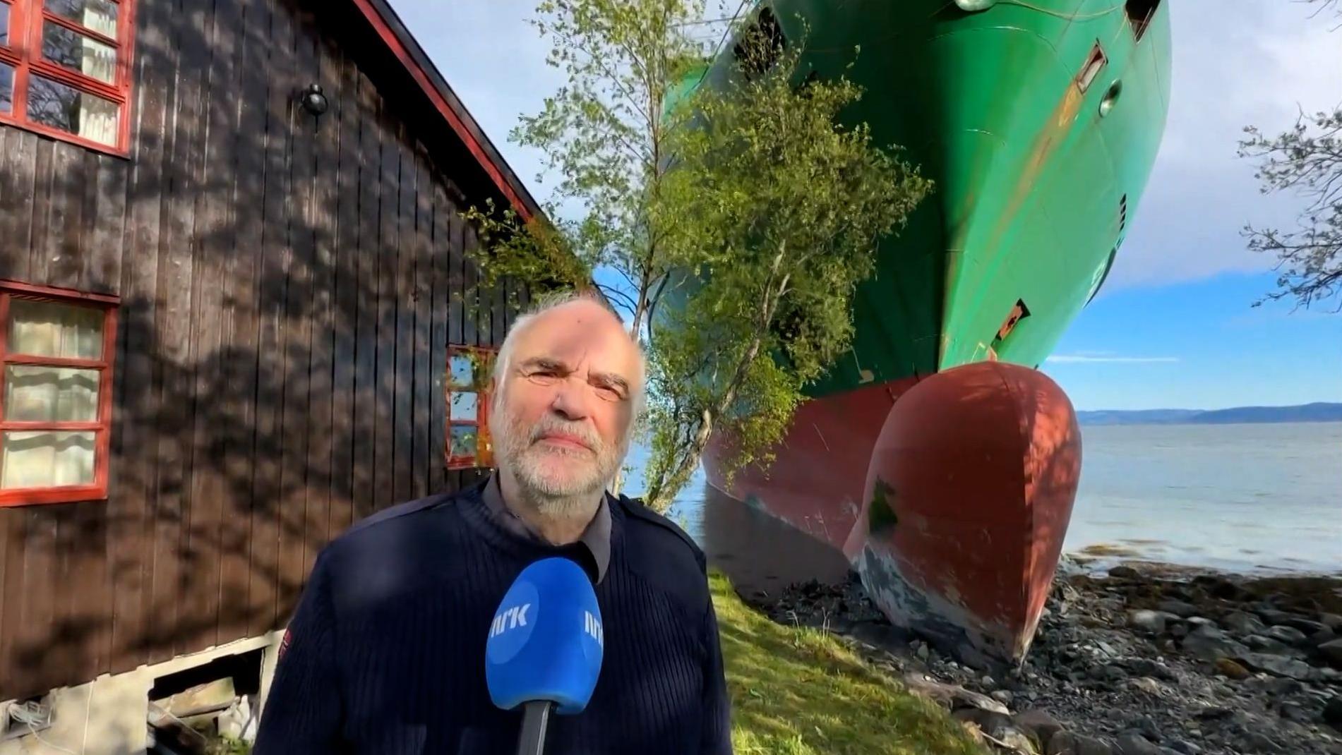 Johan Helberg habla con la televisión noruega frente a su casa y un gran buque verde encallado