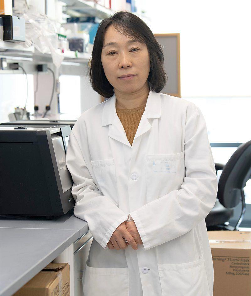 A professora Xu Yu veste um jaleco branco e olha para a c&acirc;mera com um olhar sereno, ao lado de um equipamento de laborat&oacute;rio
