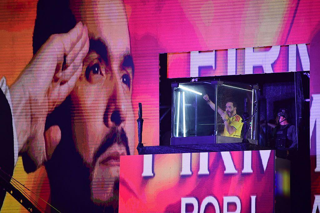 Una pantalla inmensa proyecta el rostro de Abelardo de la Espriella, con una mano firme en la frente. La cabina antibalas desde la que habla el candidato aparece en la mitad de la pantalla. De la Espriella levanta el puño derecho hacia el público.