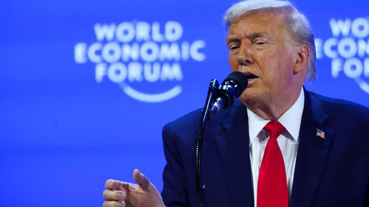 Donald Tramp u teget odelu sa crvenom kravatom dok nešto pokazuje desnom rukom